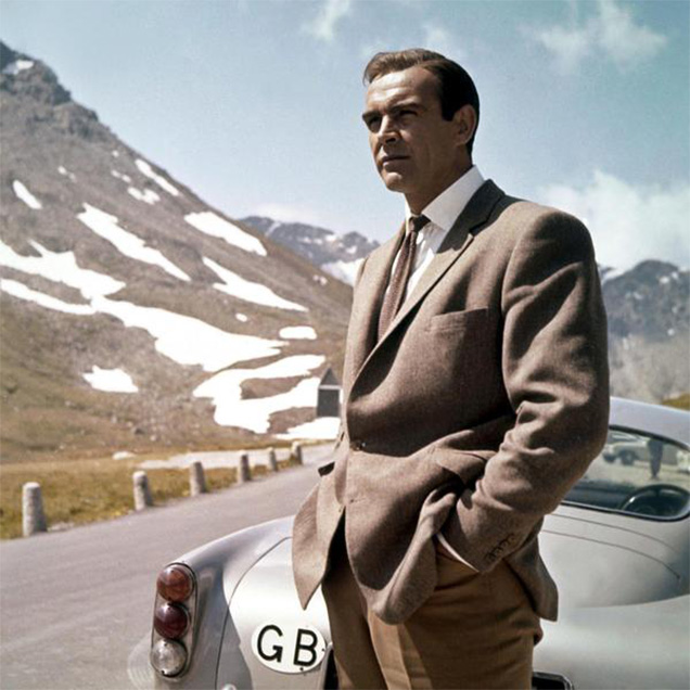 photo © Danjaq LLC, United Artists Sean Connery as James Bond wears Anthony Sinclair Barleycorn tweed hacking jacket with Cavalry Twill Trousers during the car chase in Goldfinger.